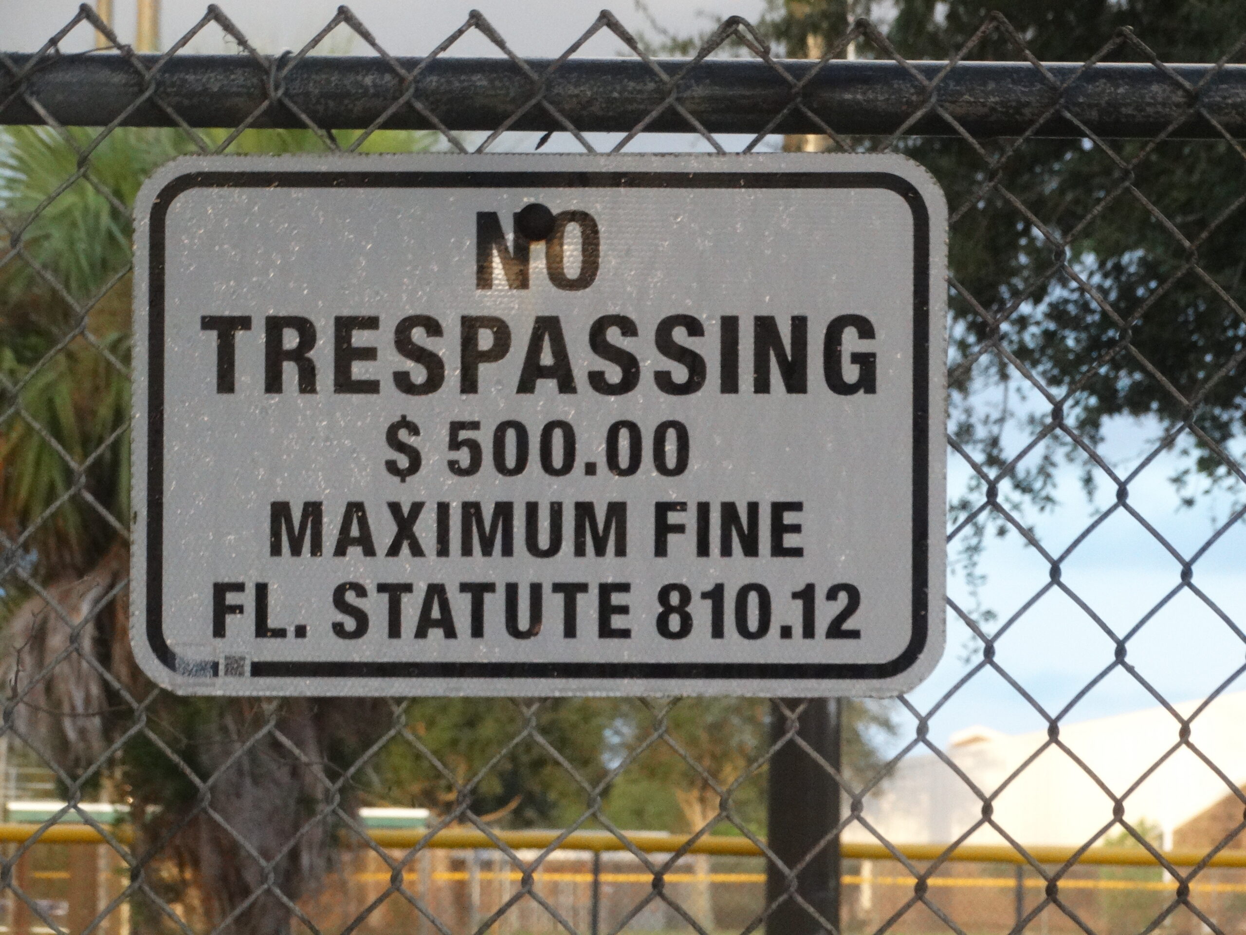 closeup of no trespassing warning sign on chain link fence